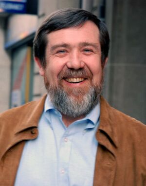 A cropped headshot of Alexey Pajitnov smiling, standing outside of a building during the day.